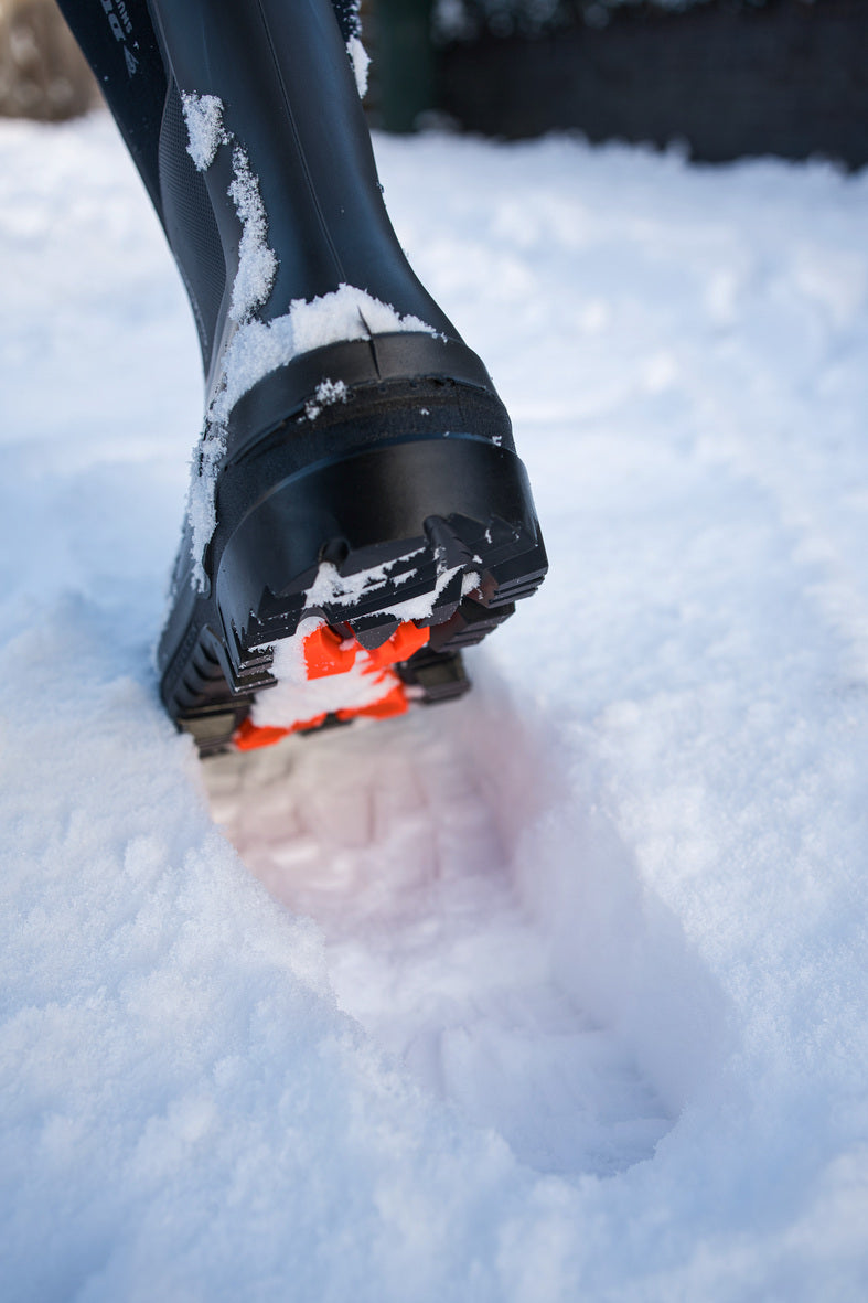 Bota Dunlop Snugboot Heavy Duty Calf Full Safety Media Caña para Trabajos Pesados pisando la nieve con ángulo izquierdo