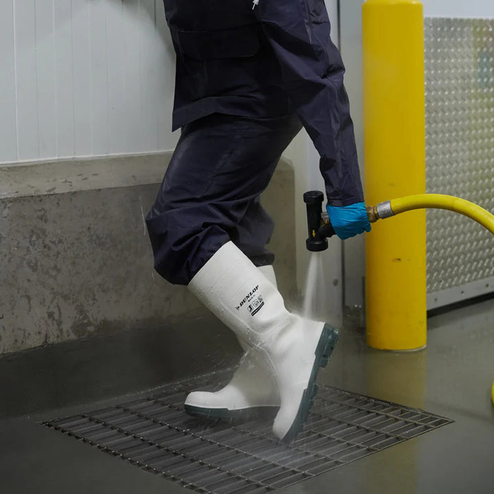 Persona lavando las botas Dunlop Work-It S4 (Blanco) calzadas con una maguera